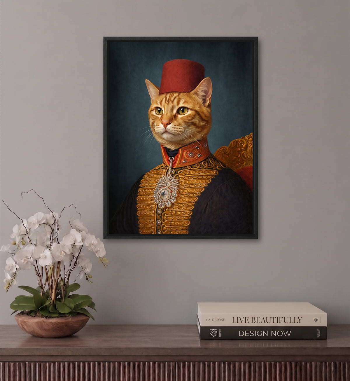 a cat wearing a red fez hat and a gold and black outfit, with a potted plant and a stack of books on a wooden surface below the framed picture.