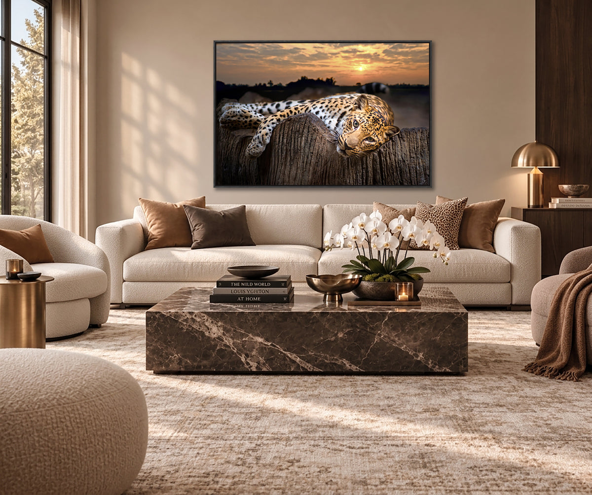 a living room with a large framed photograph of a leopard resting on a wooden fence. The room has a neutral color scheme with beige sofas, a marble coffee table, and a large window providing natural light.
