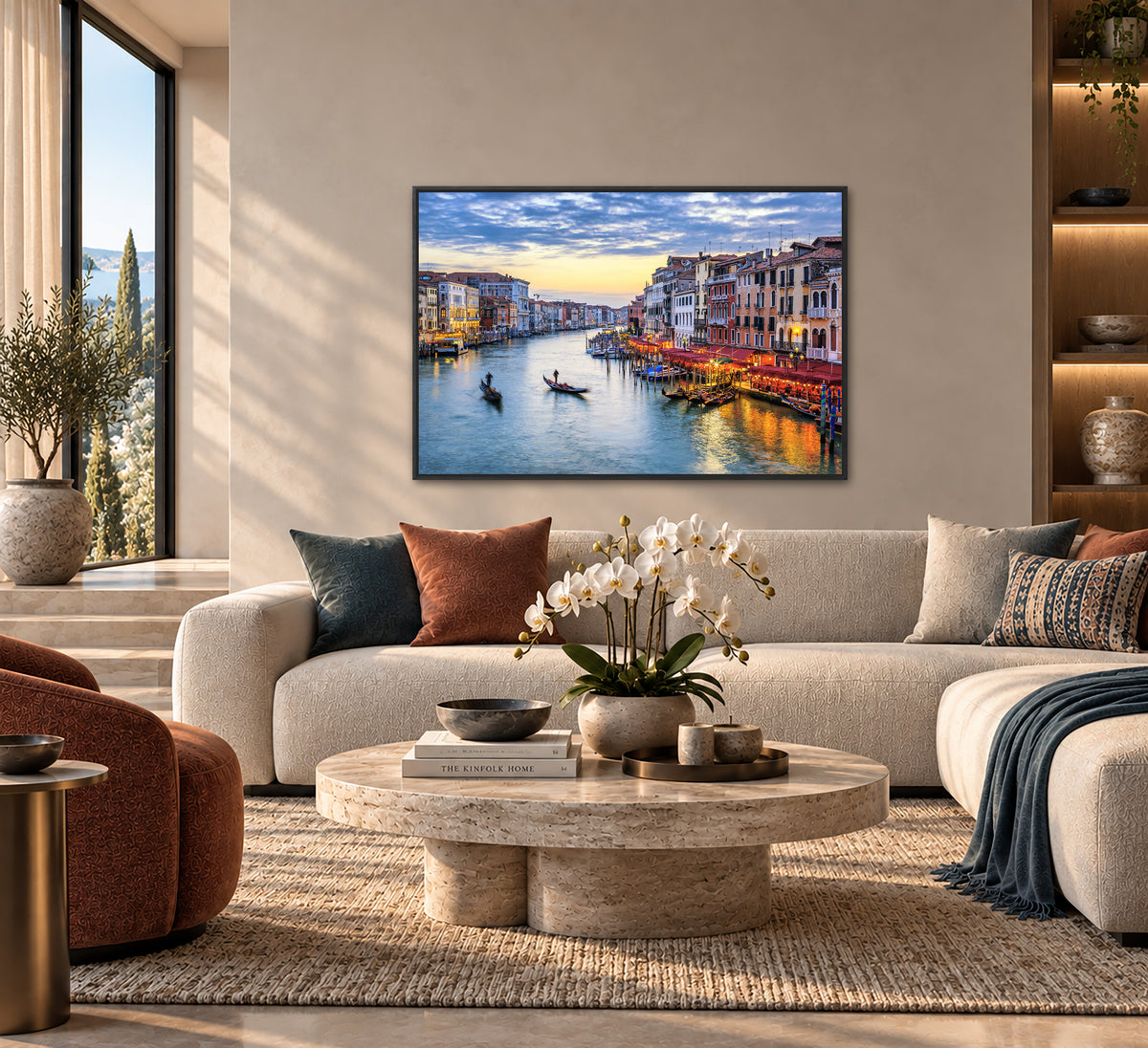 a modern living room with a large window overlooking a picturesque canal scene in Venice, Italy. The room is furnished with a white sofa, a round coffee table, and a bookshelf. A framed photograph of the canal and the surrounding buildings is prominently displayed on the wall, adding a touch of color and life to the space.